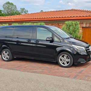 Juodas Mercedes-Benz V-Klasės mikroautobusas pastatytas kieme prie namo,