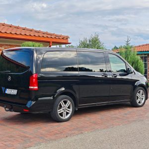 Juodas Mercedes-Benz V-Klasės mikroautobusas pastatytas kieme prie raudonų plytų namo